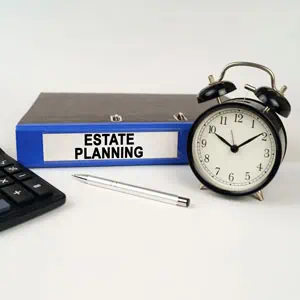 Estate planning is written on the file on the table, along with an alarm clock, a pen, and a calculator. - The Greene Law Firm, P.A