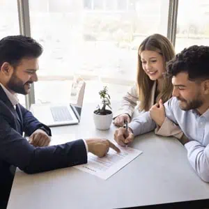 Three individuals discussing a document at a table, focusing on trust structure for a family member with addiction