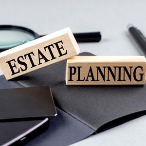 Wooden blocks spelling 'ESTATE PLANNING' with magnifying glass and pen.